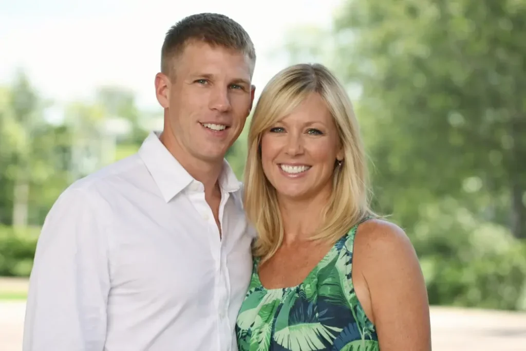 Denika Kisty smiling outdoors alongside her husband Jason Williams in a bright setting.